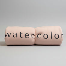 Load image into Gallery viewer, Rolled-up pink blanket with 'watercolor' text on a wooden surface in a store setting.